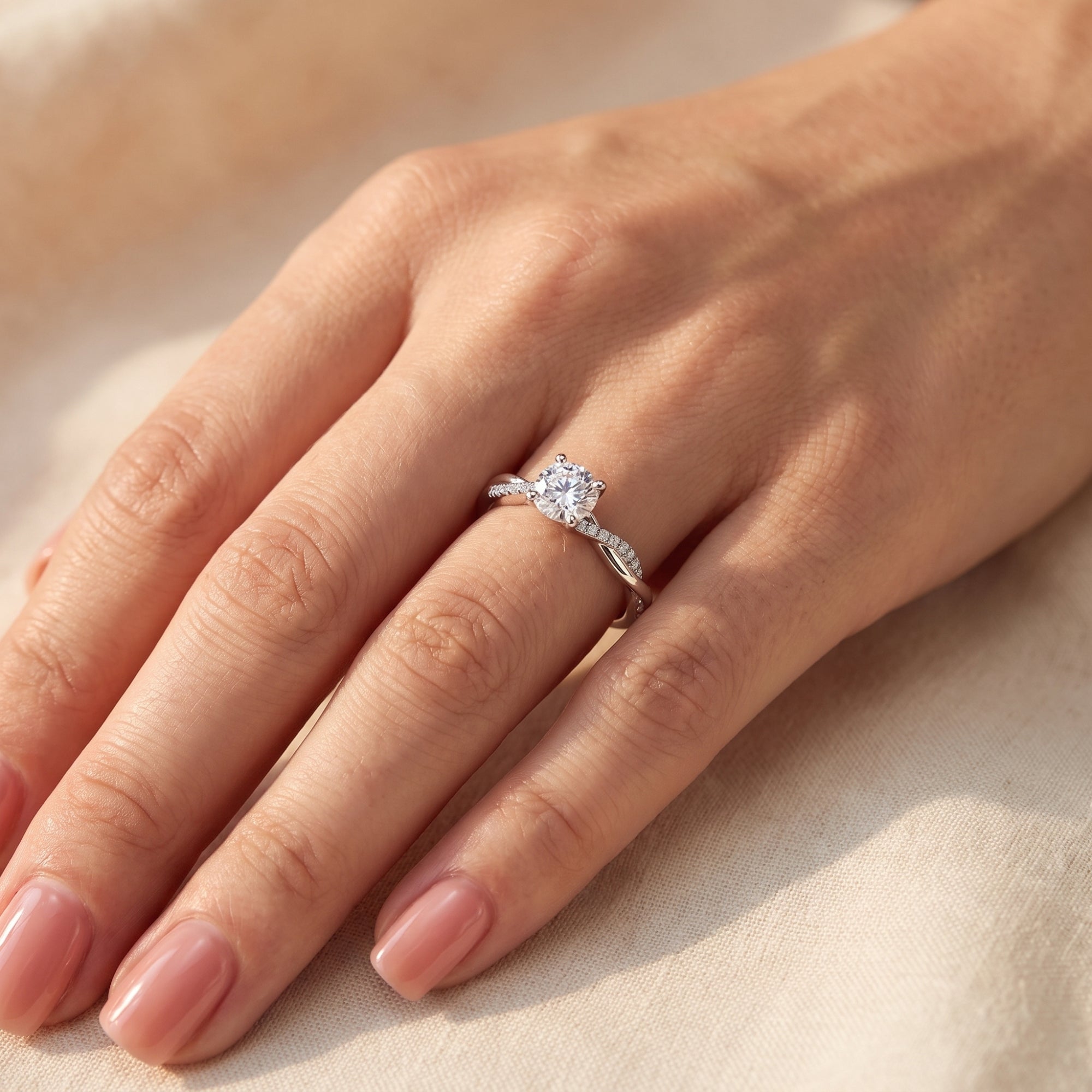 Round-cut simulated diamond solitaire ring in sterling silver worn on a woman's hand against light fabric.