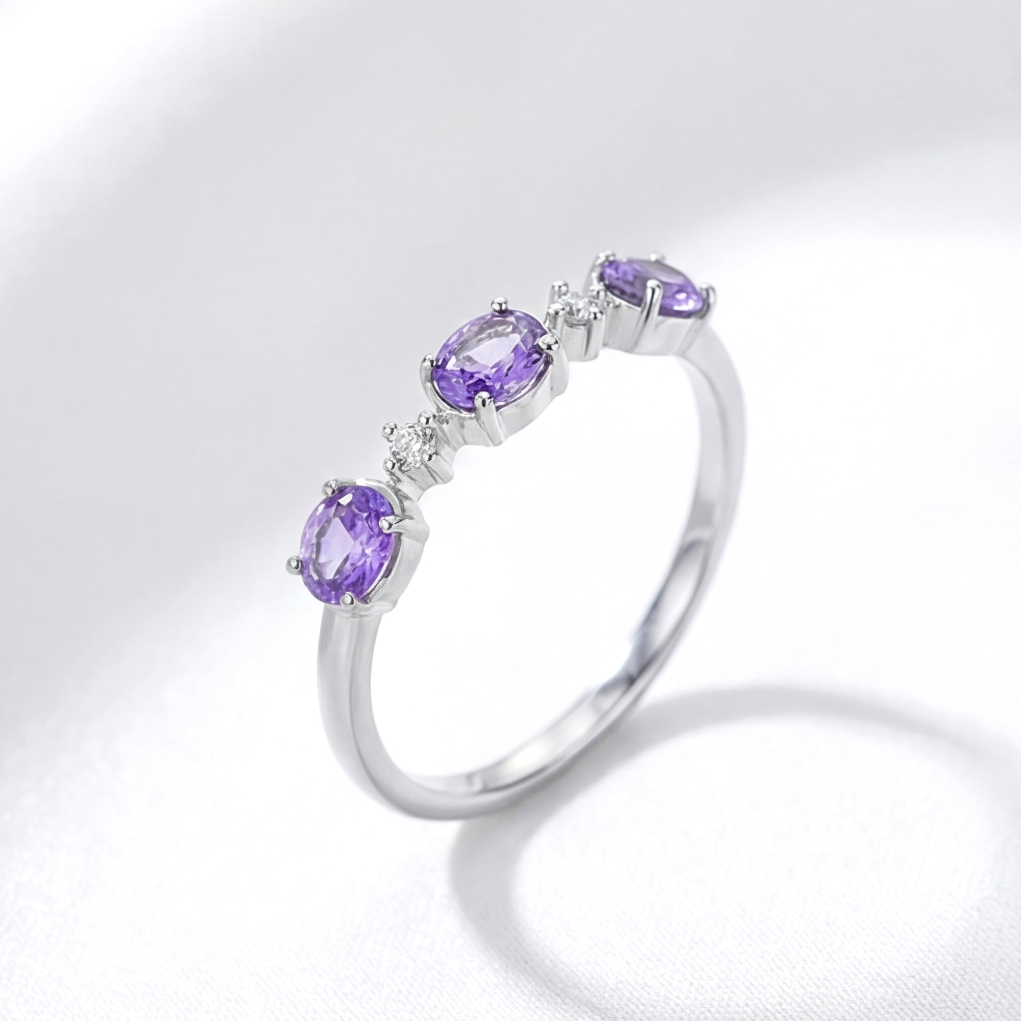 Angled side view of the Serenitas S925 sterling silver ring with oval simulated amethysts on white fabric.