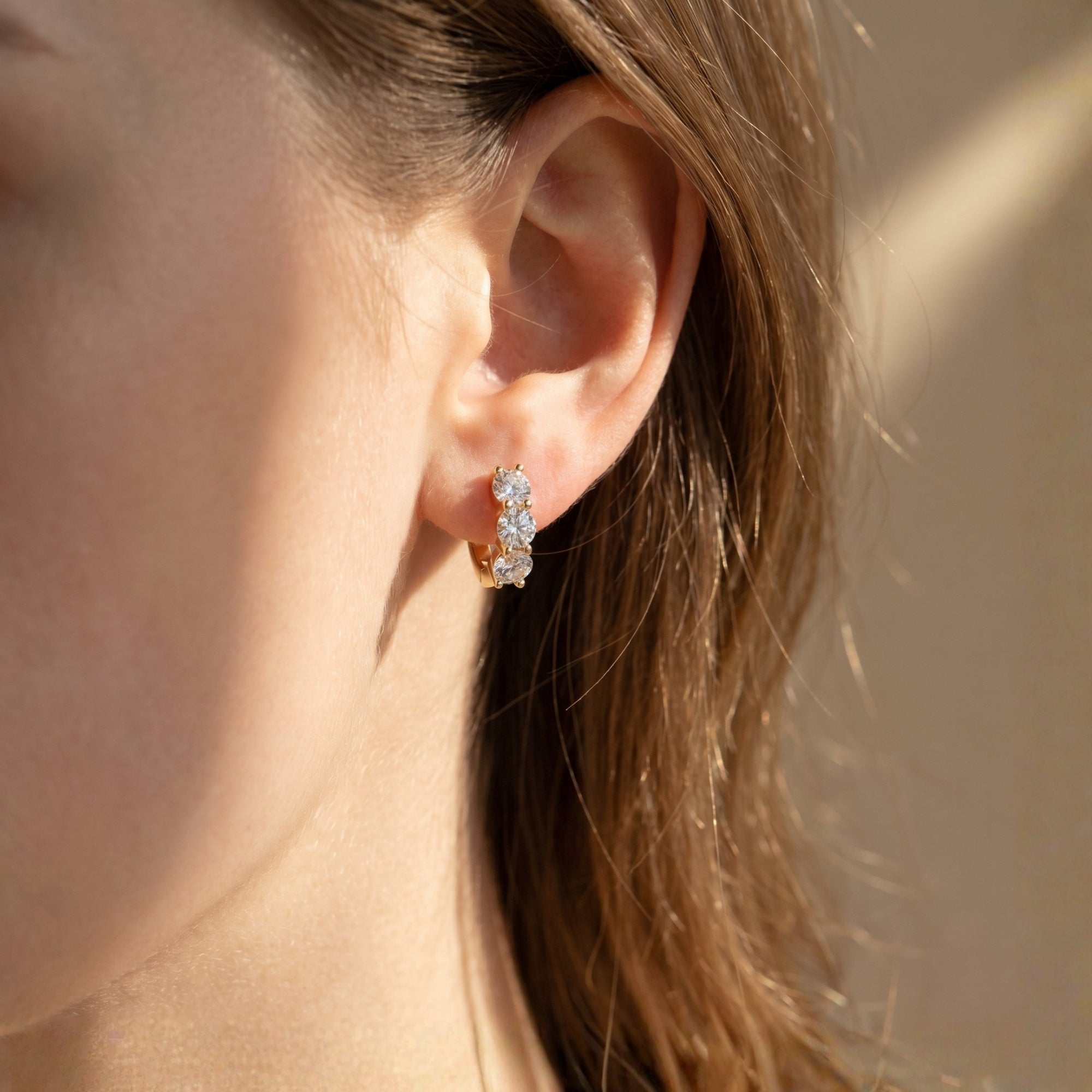 Gold moissanite hoop earring featuring three round stones worn on a woman's ear.
