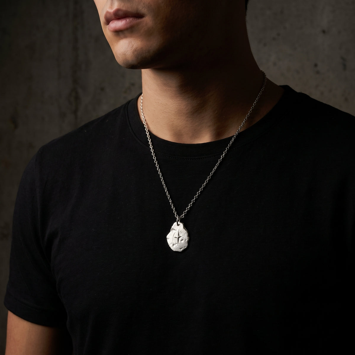 Front view of a man wearing the silver starburst pendant necklace over a black T-shirt.