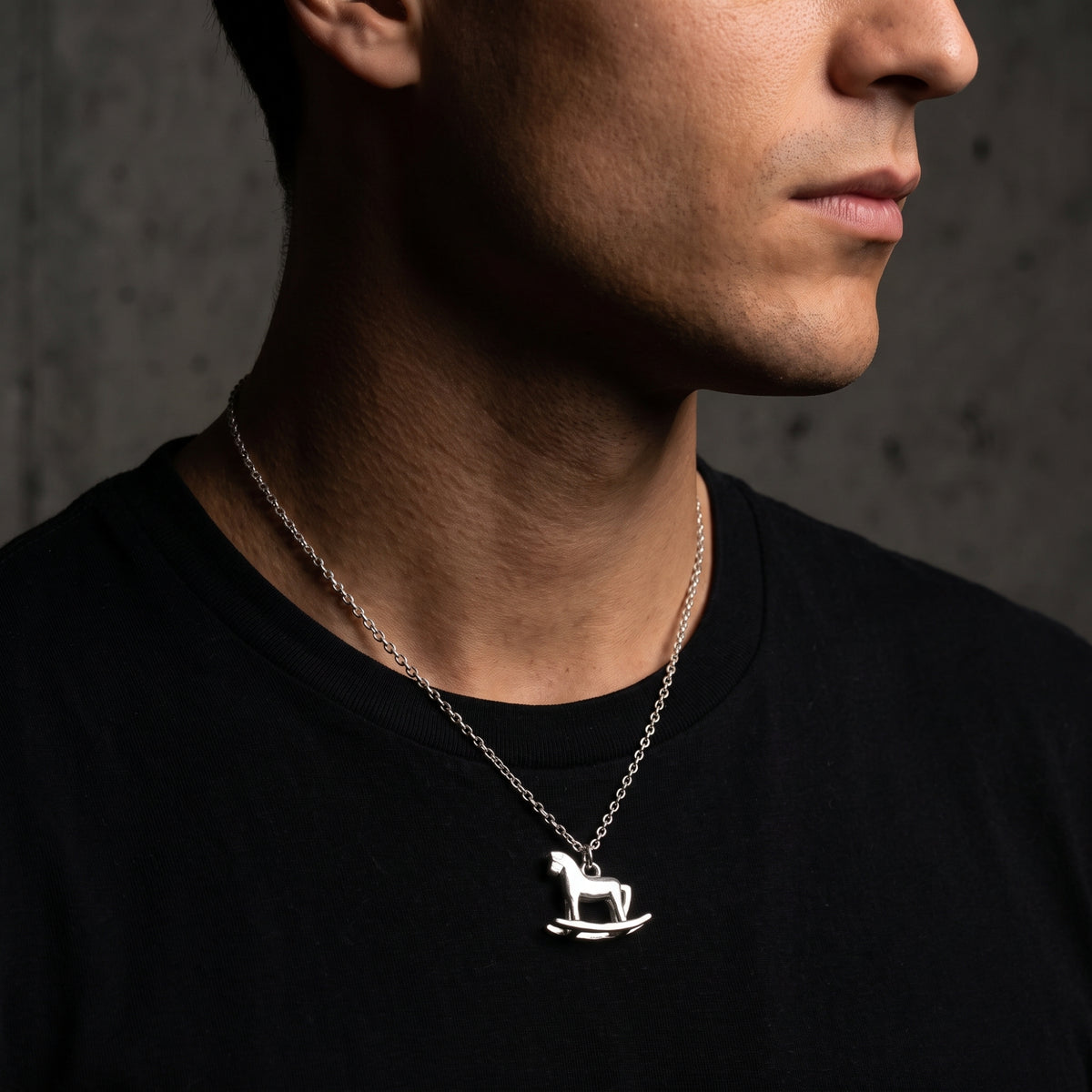Side-profile close-up of a model wearing the silver rocking horse pendant necklace over a black T-shirt.