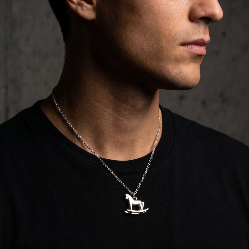 Side-profile close-up of a model wearing the silver rocking horse pendant necklace over a black T-shirt.