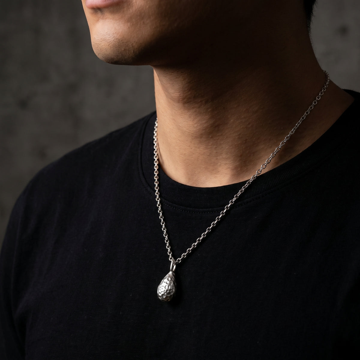 Close-up of a person wearing the textured silver teardrop pendant over a black shirt.