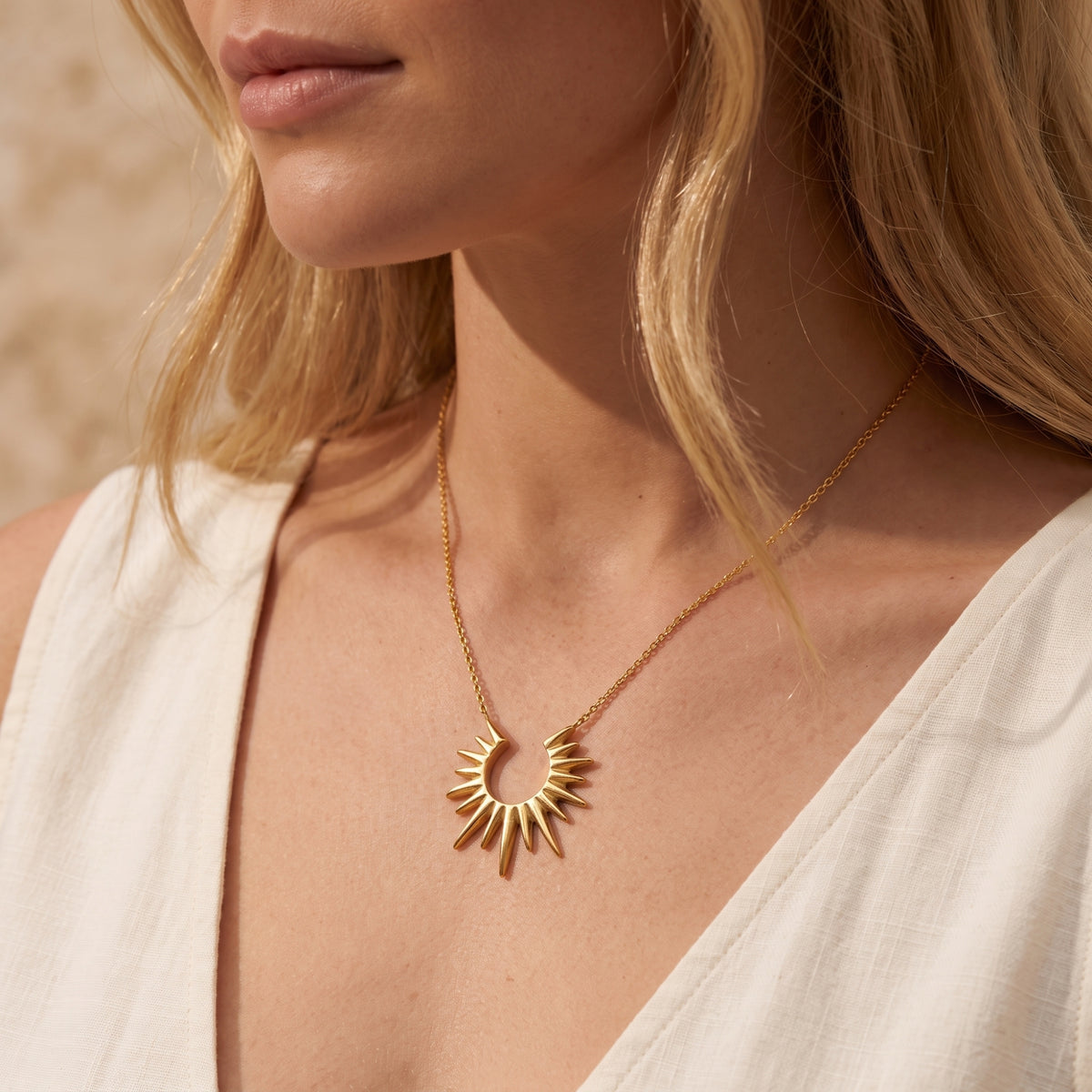 Side-angle model view showcasing the gold-toned sunburst pendant necklace worn against a white top.