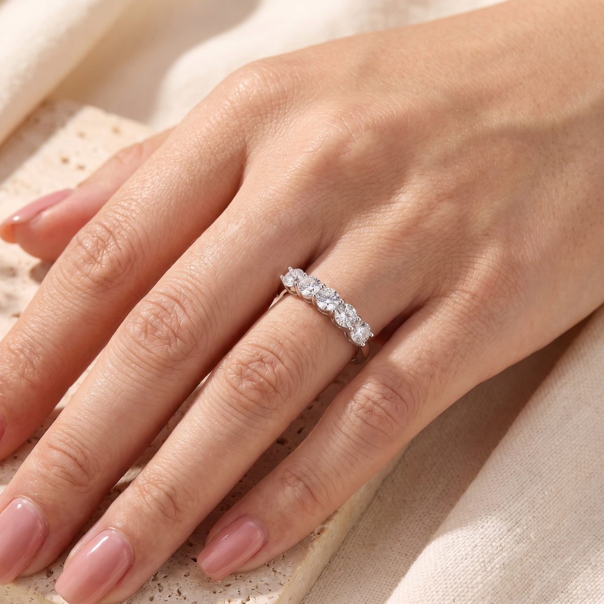Silver five-stone ring with round clear stones worn on a hand resting over a stone block.