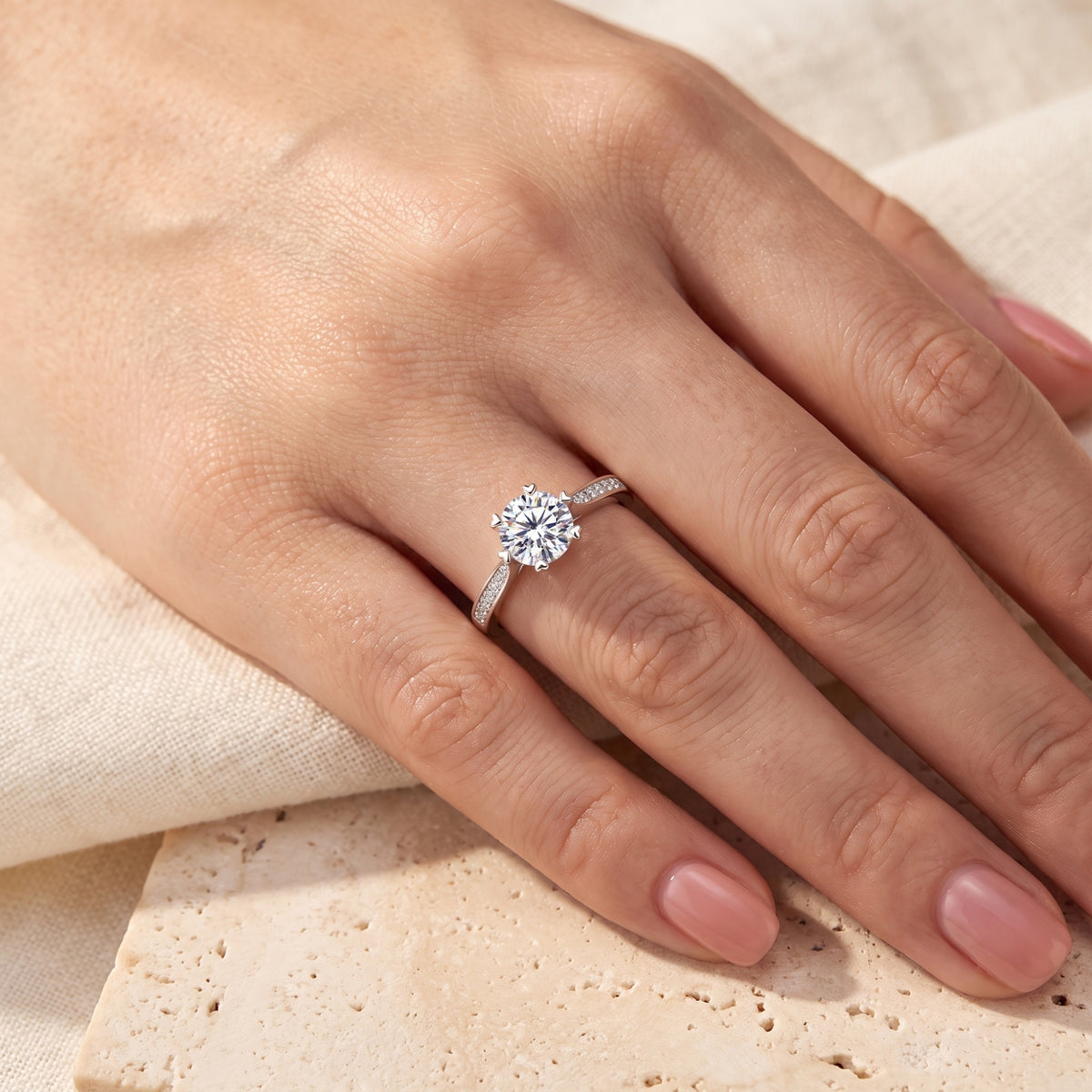 Silver cathedral ring with a round clear gem worn on a hand resting on stone and fabric backgrounds.