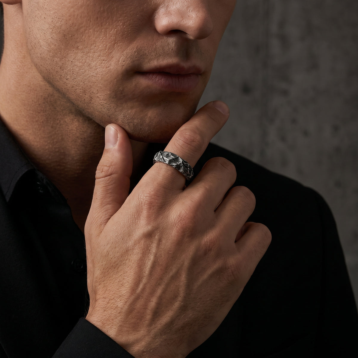 A man wears the carved silver open-band ring on his index finger while resting his hand on his chin.