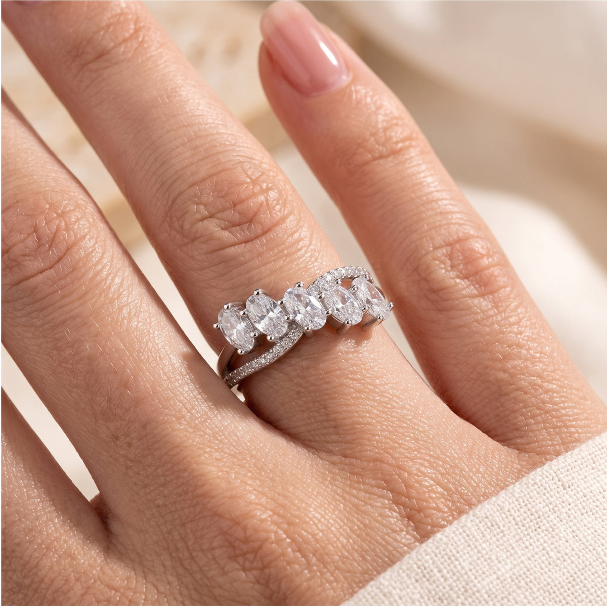 Silver bypass ring worn on a finger, showing five oval clear stones and pavé accents along the split band.