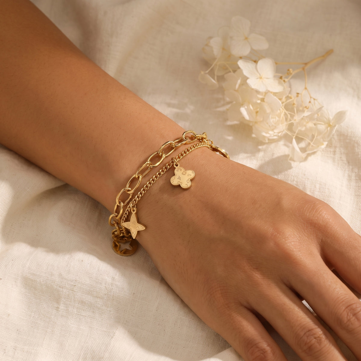 Close-up of the gold-tone double-chain clover and star charm bracelet worn on a wrist.