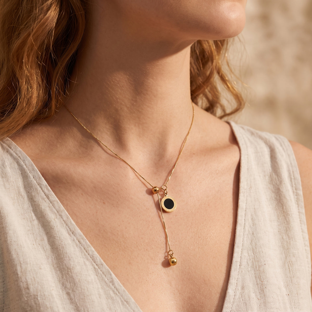 Gold-tone lariat necklace with black Roman numeral disc pendant worn on a model in a light beige sleeveless top.