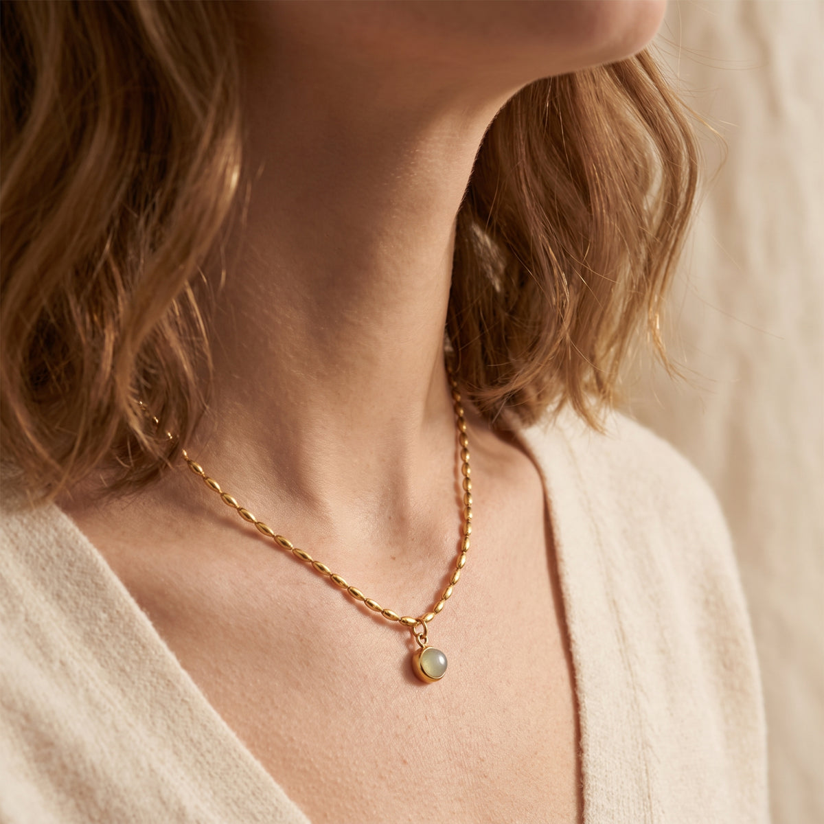 Angled close-up of a model wearing the gold-tone oval-bead necklace and round bezel-set pendant.
