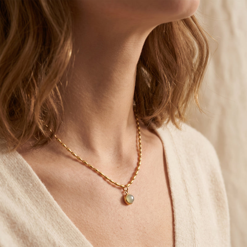 Angled close-up of a model wearing the gold-tone oval-bead necklace and round bezel-set pendant.