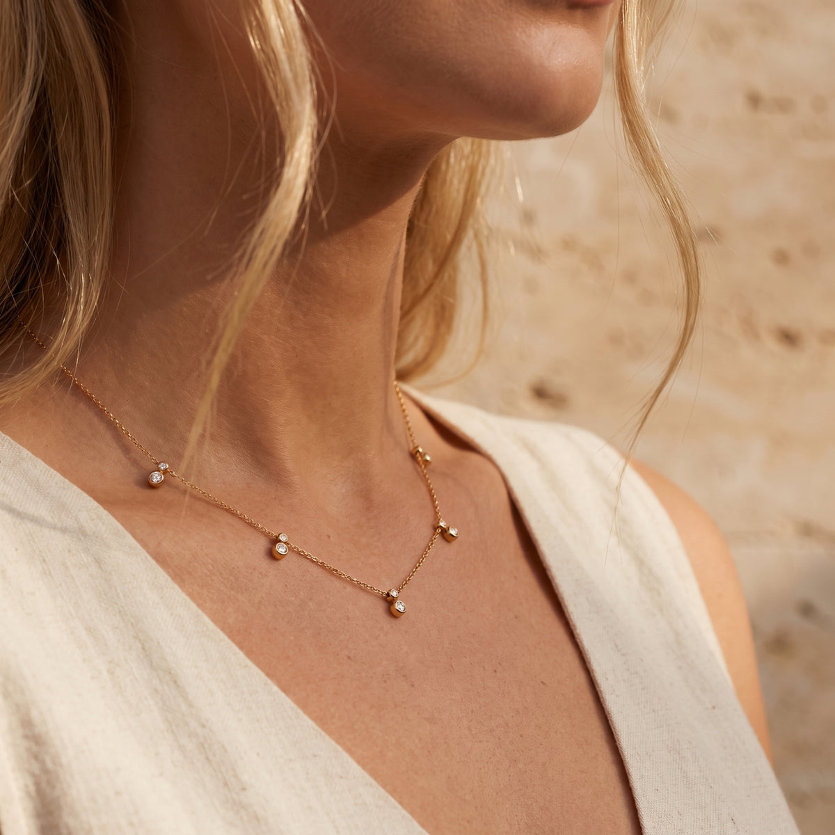 Side view of a model wearing the gold-tone bezel station necklace over an off-white top.