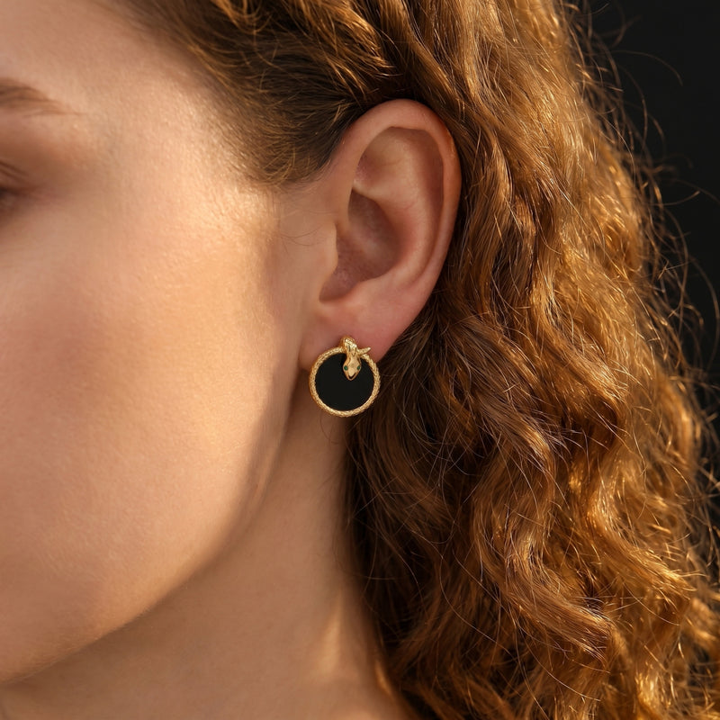 Model wearing a gold plated Serpens onyx earring featuring a snake head design with green eyes.