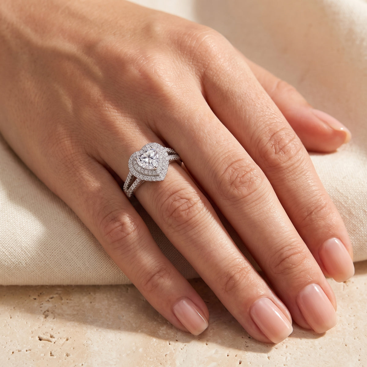 Heart-shaped double-halo silver ring worn on a finger, viewed from above.
