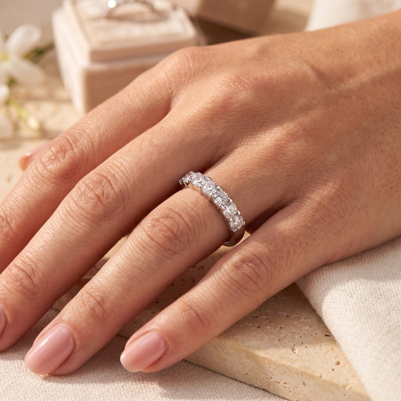 Seven-stone silver ring with round clear stones worn on a finger.