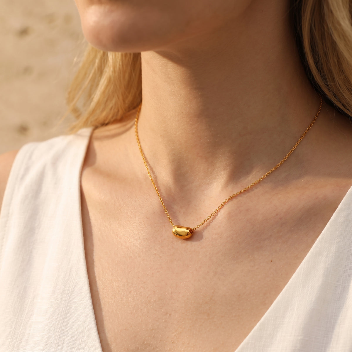 Model wearing the gold-toned sculpted pod necklace over a sleeveless white V-neck top.