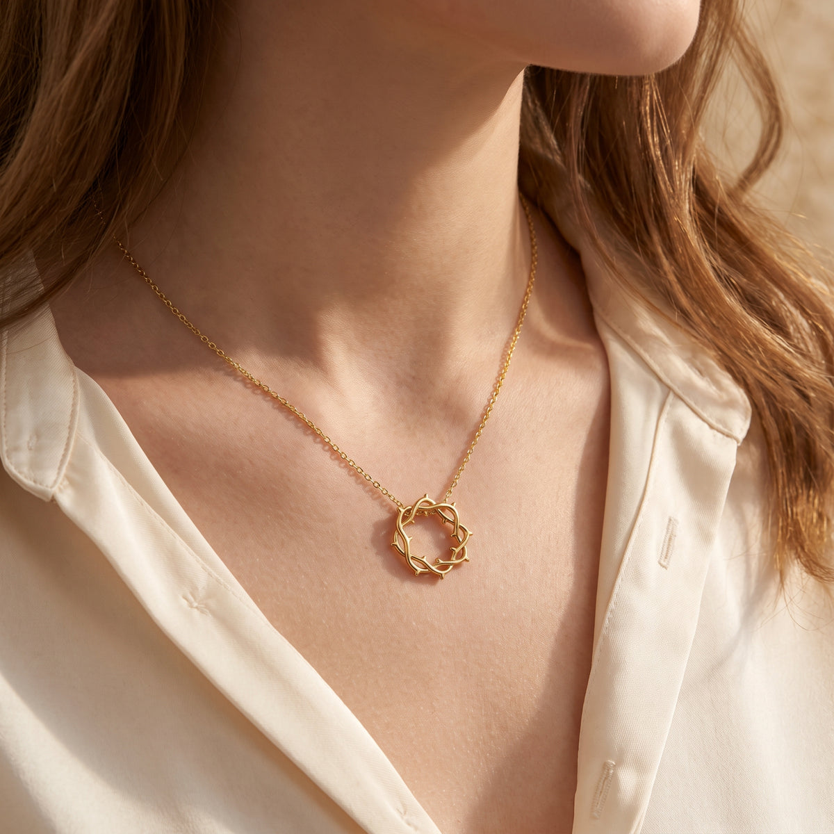 Gold crown of thorns necklace worn on a model over an open-collared cream shirt.