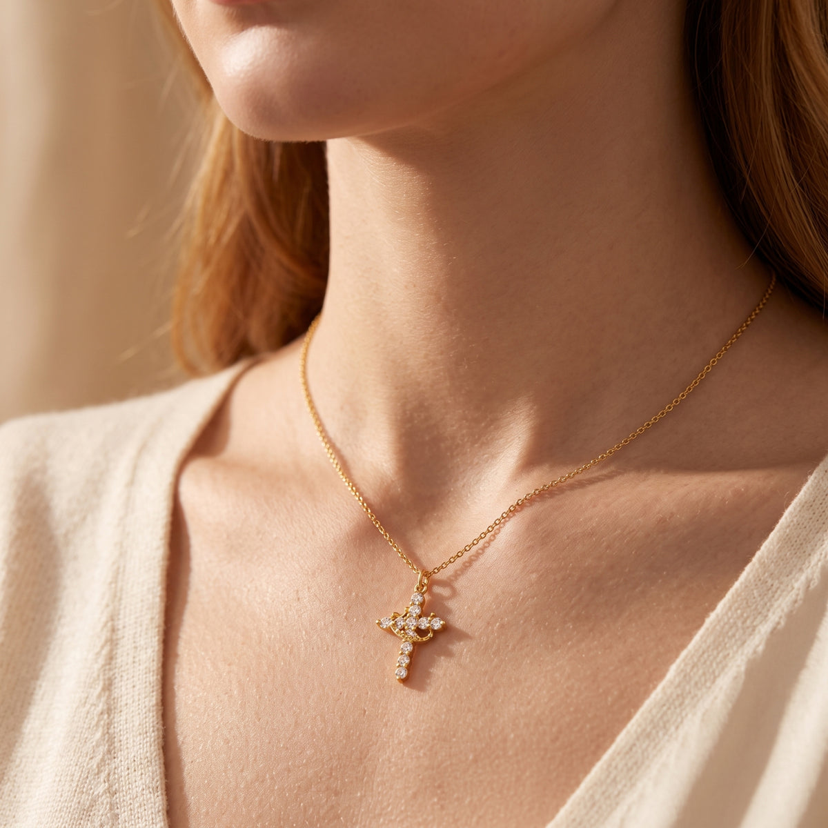 Close-up of a model wearing the gold-tone crown cross necklace against a light beige sweater.