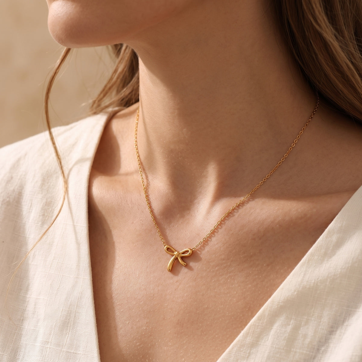 Model wearing the gold-tone bow pendant necklace with a white V-neck shirt.