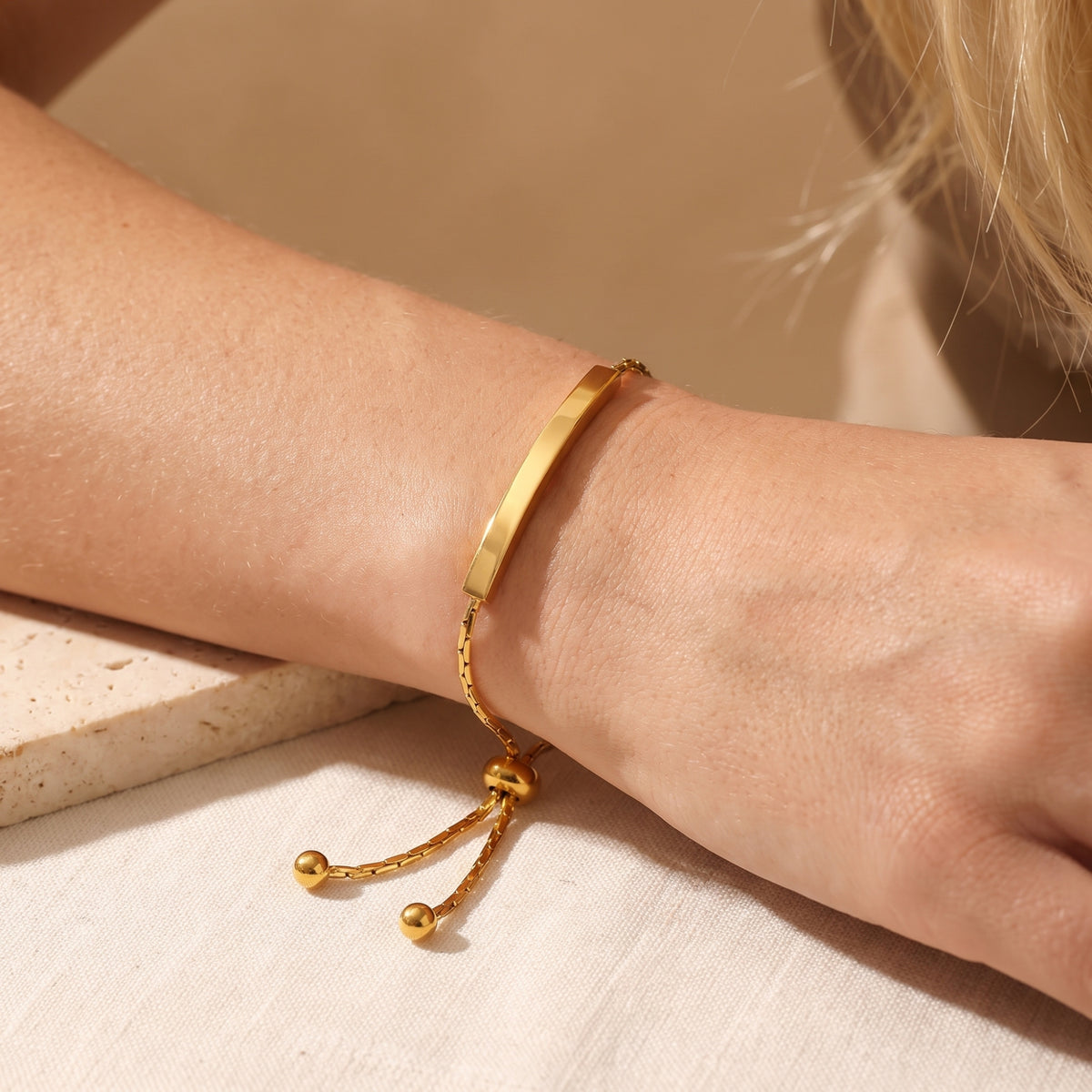 Close-up of a gold-tone curved bar slider bracelet worn on a wrist, with the slider bead and chain ends hanging below.