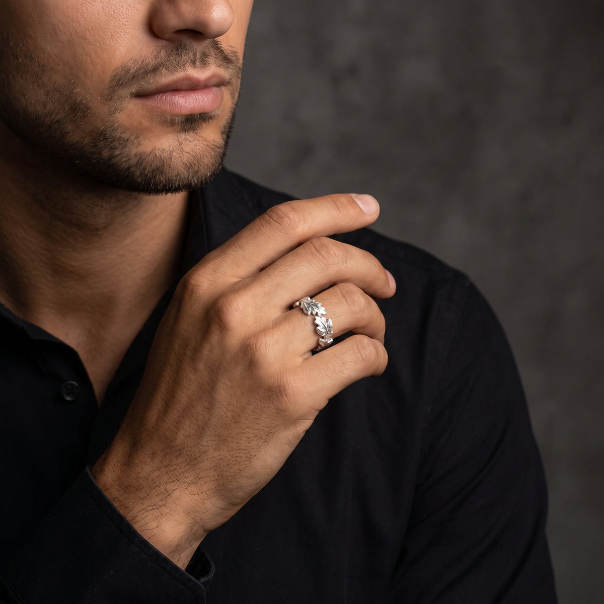 Silver oak leaf ring worn on a man's ring finger against a dark shirt.