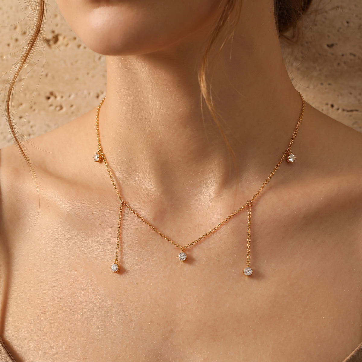 Gold-tone five-drop necklace with clear stones worn on a model’s neck and collarbone in close-up.