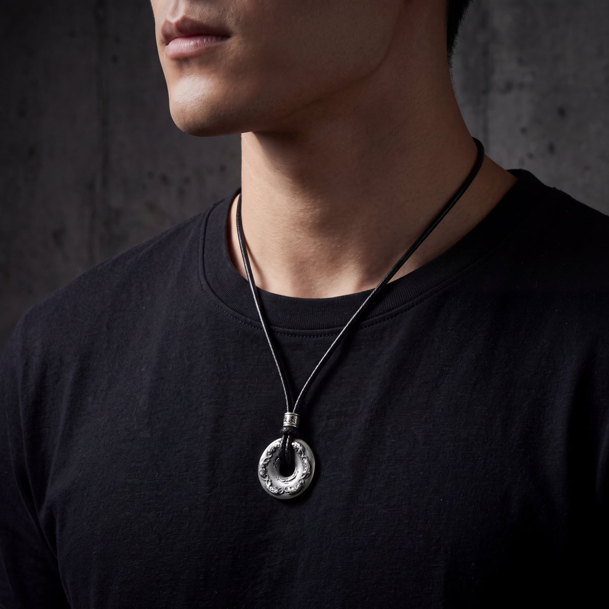Close-up of a man wearing the antiqued silver carved disc pendant necklace on a black cord.