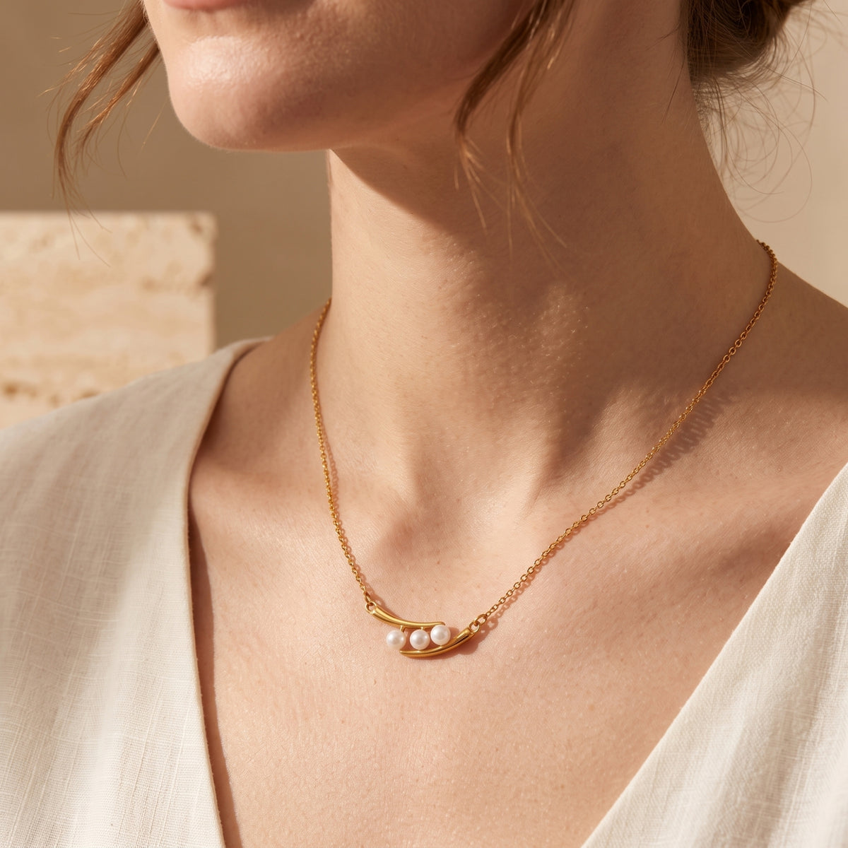 Close-up of a model wearing the gold-tone necklace with three simulated pearls against a white top.