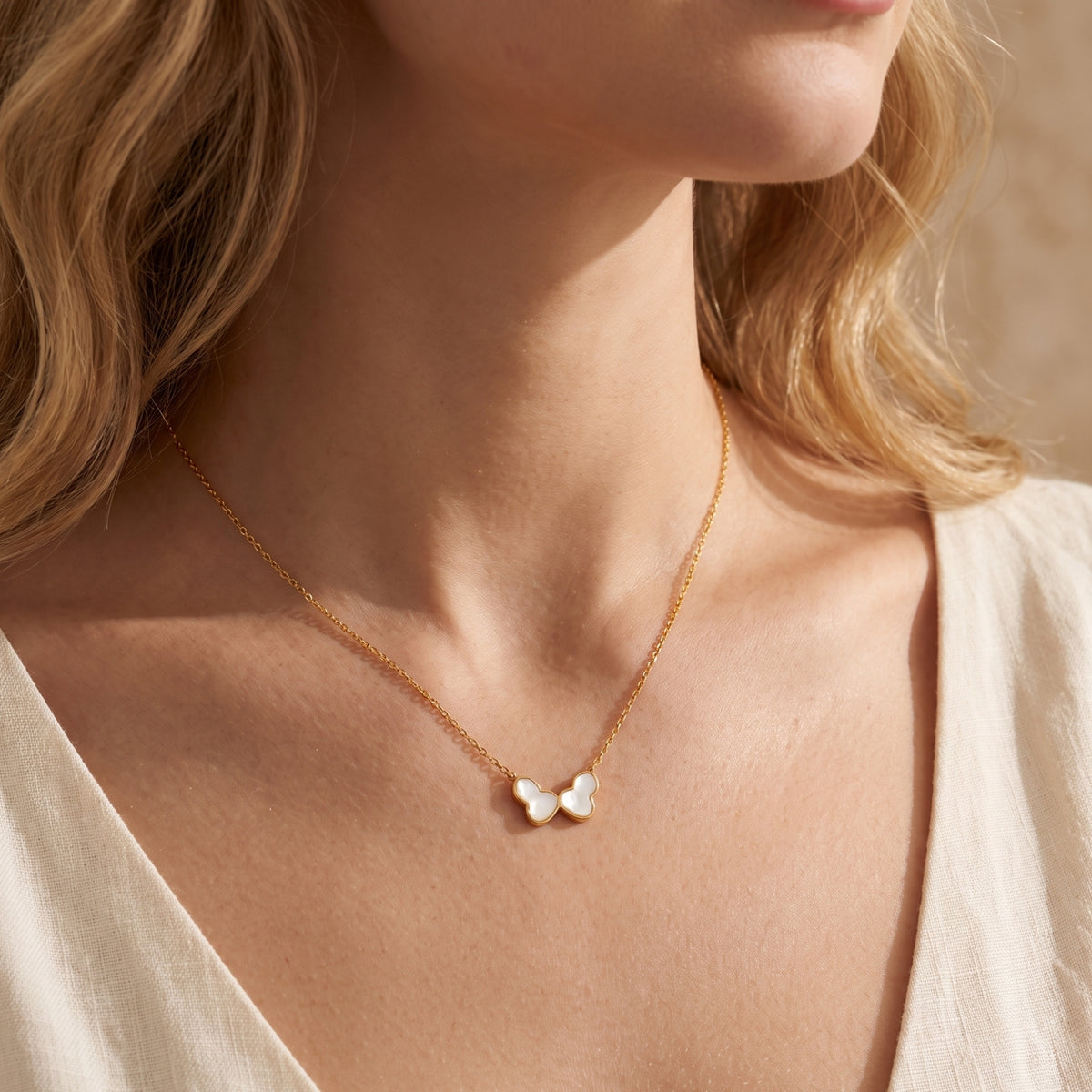 Model wearing a gold-tone necklace with a white iridescent butterfly pendant against a white V-neck top.