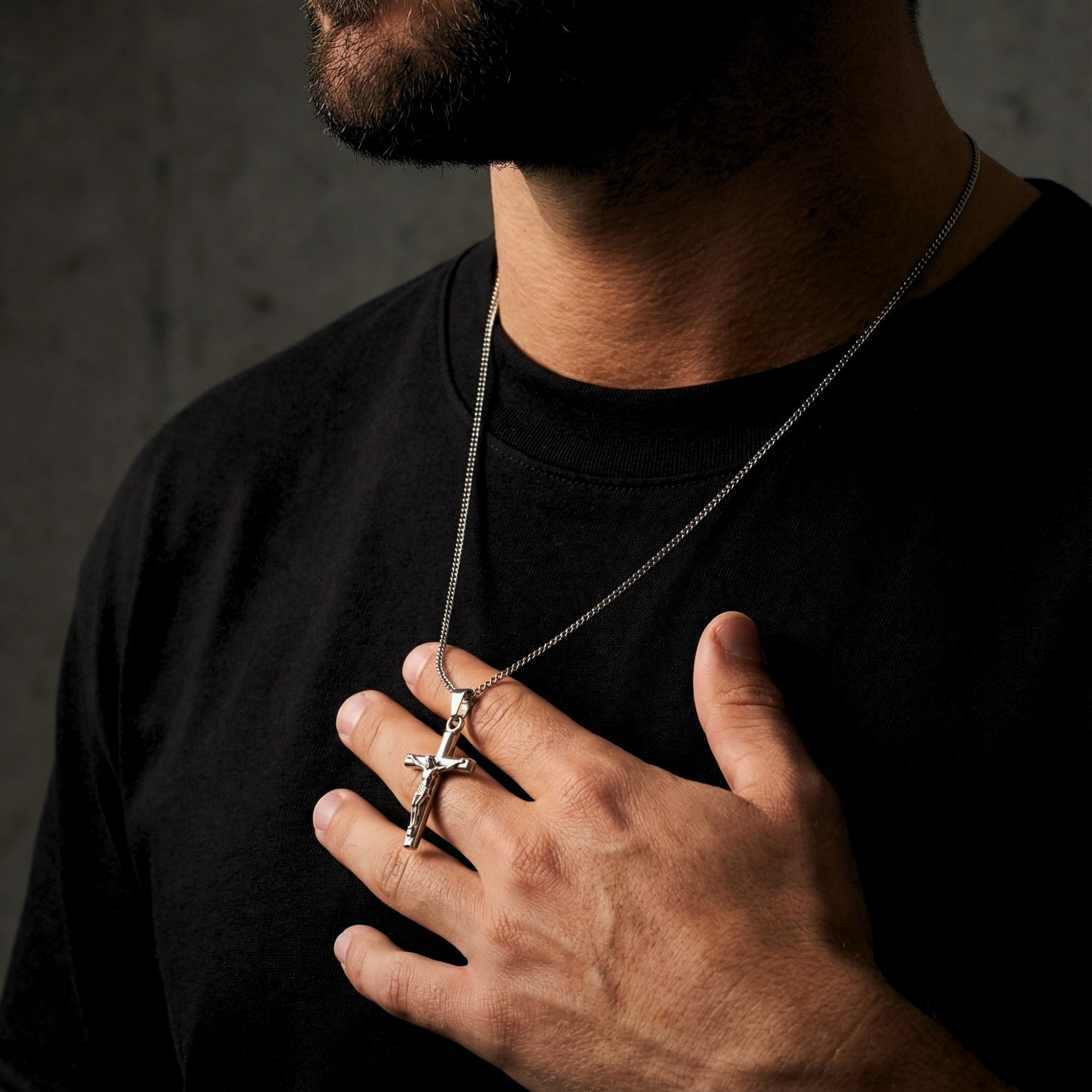 Man holding the silver stainless steel crucifix pendant to show its size and scale against a black shirt.