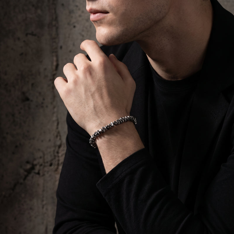 On-model view of a man wearing the silver pebble link bracelet while resting his chin on his hand.