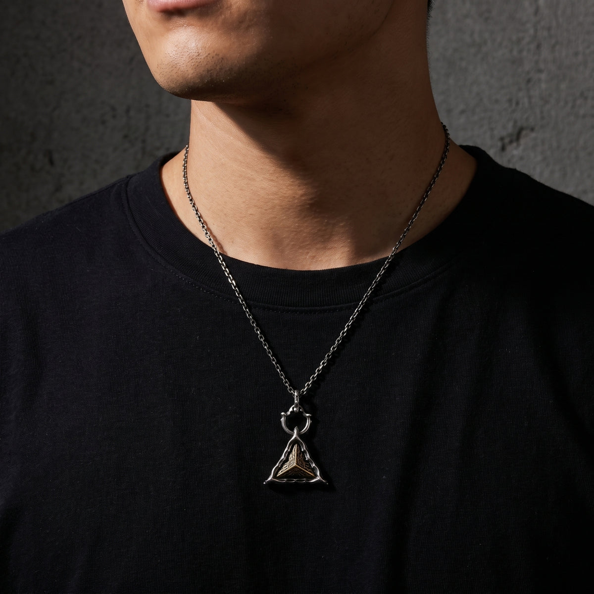 Man wearing the silver triangular pendant necklace centered over a black crew-neck shirt.