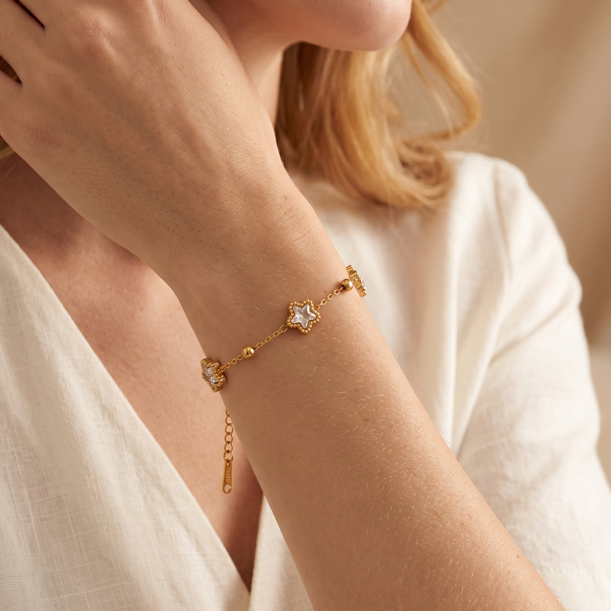 Woman wearing the gold-tone star station bracelet on her wrist against a white top.