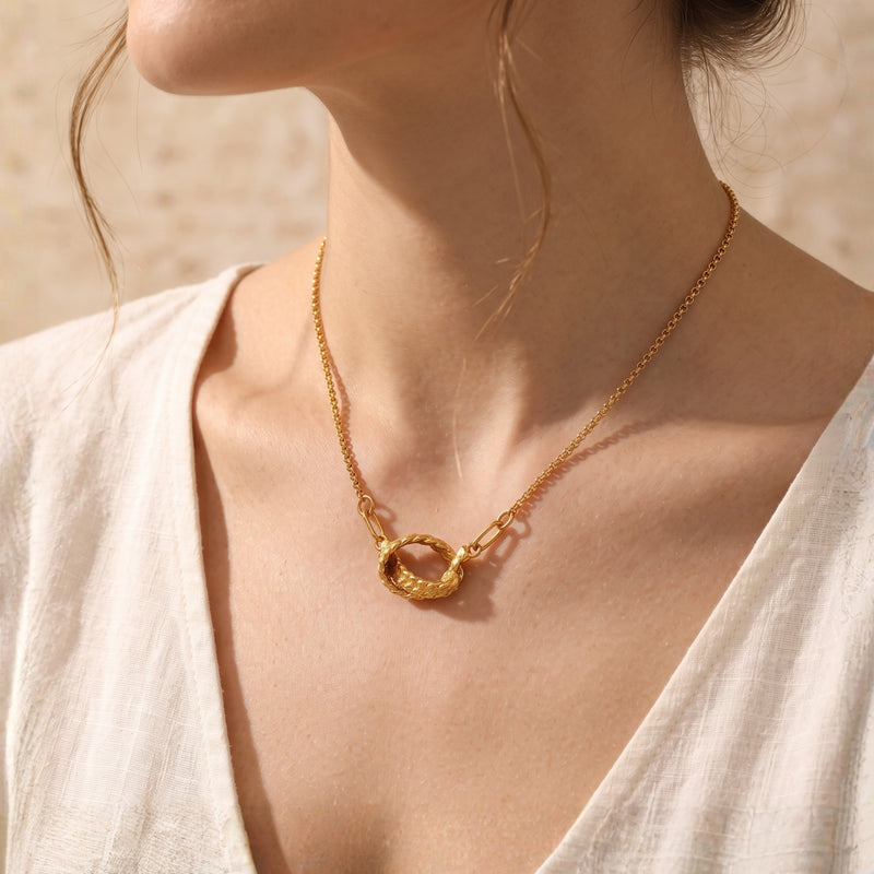 Model wearing the gold Vincenza braided knot necklace with a white top.