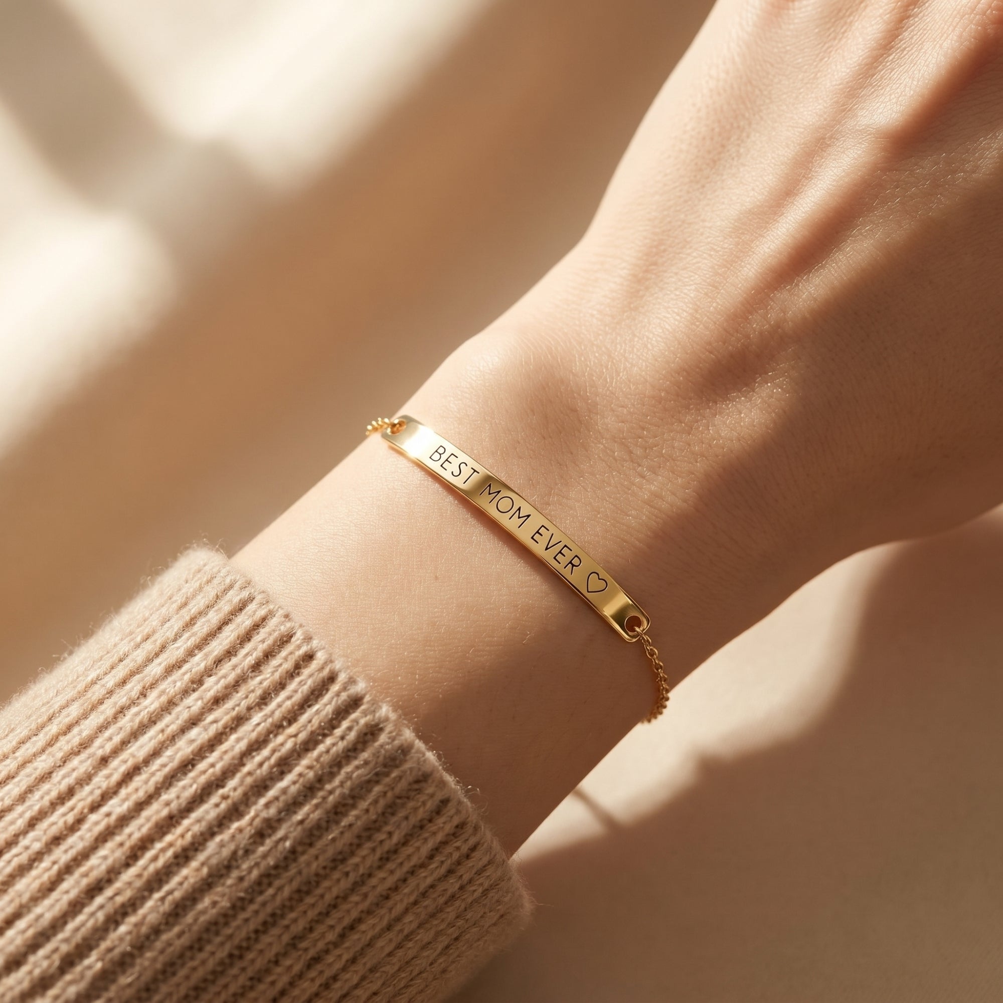 Gold Eleanor Bar Bracelet engraved with BEST MOM EVER worn on a woman's wrist over a beige sweater.