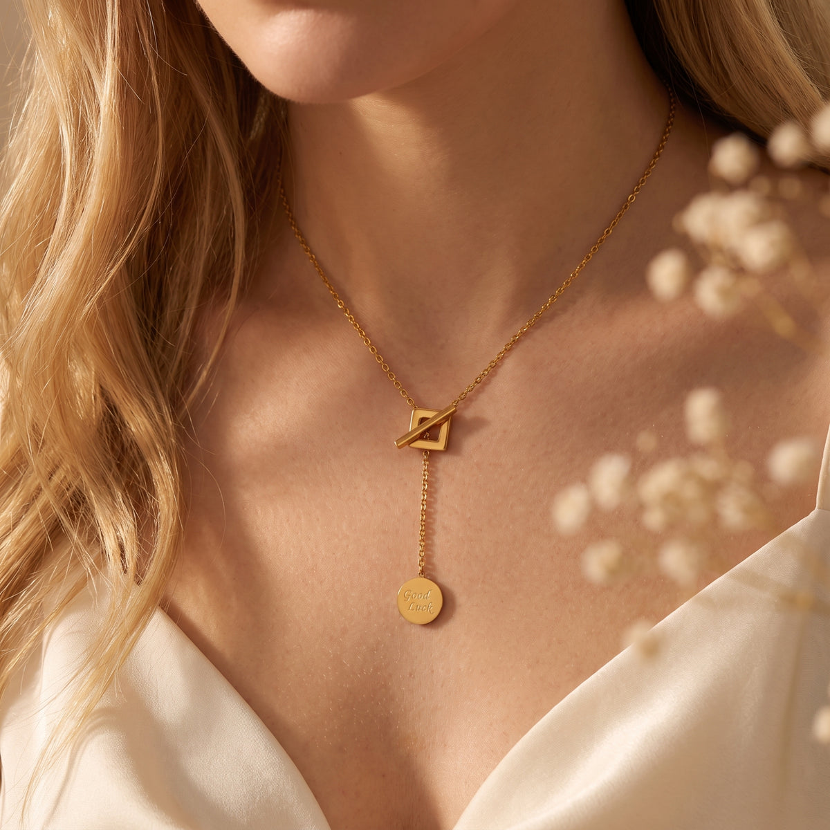 Close-up model view of gold-tone lariat necklace with square toggle and dangling Good Luck coin pendant.