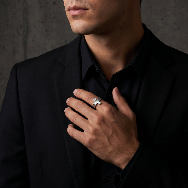 Man in a black suit wears the textured cross ring on a finger while resting his hand against his chest.