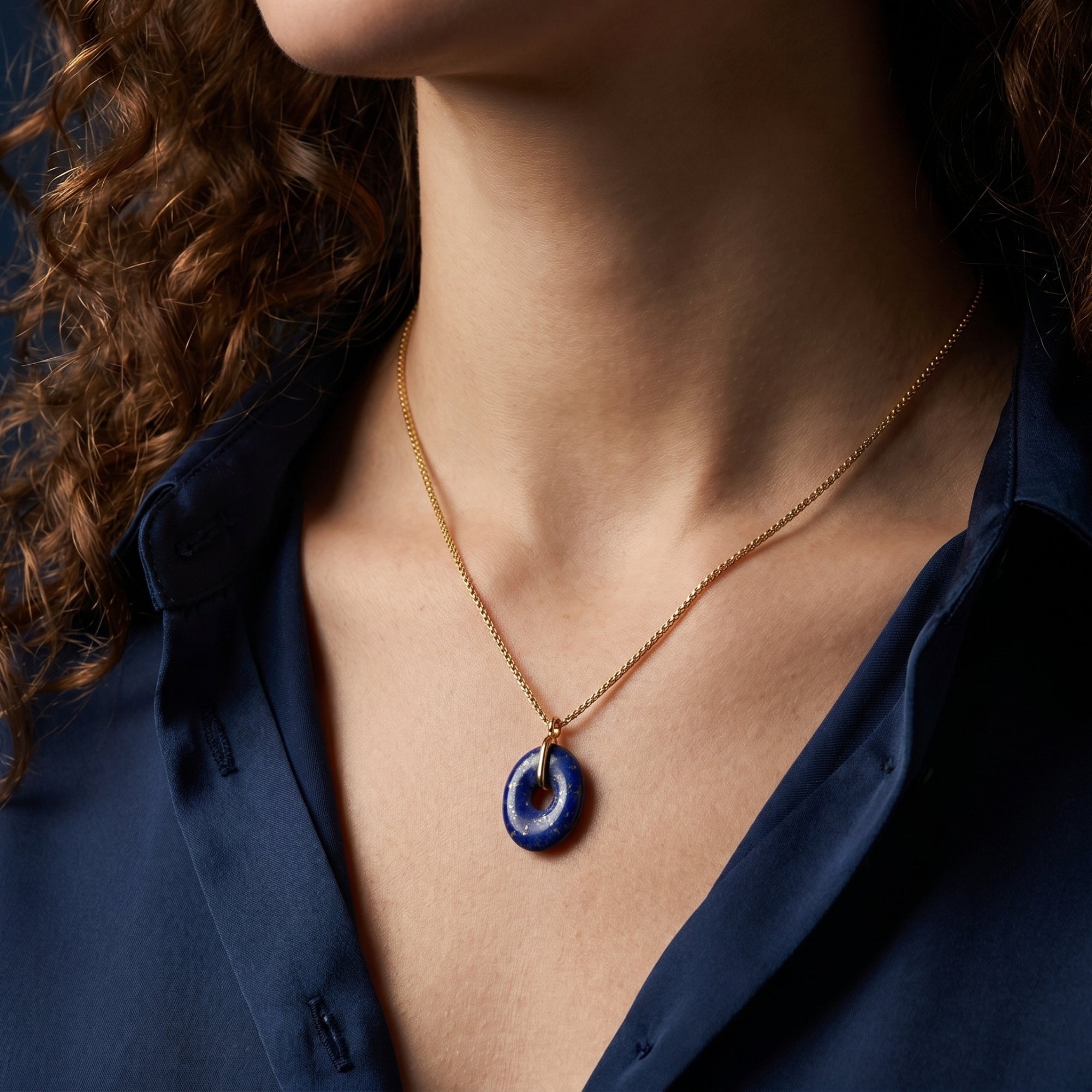 Model wearing the gold plated Odyssey necklace with an oval natural lapis lazuli pendant over a blue shirt.