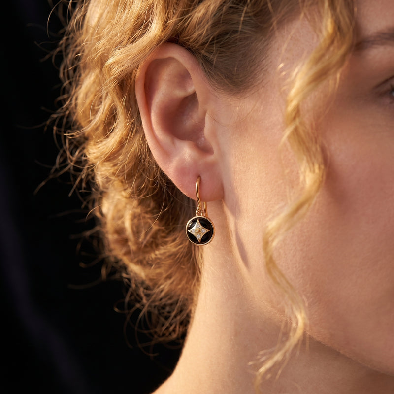 Close-up of a model wearing a yellow gold drop earring with a round black onyx and star-shaped diamond accent.