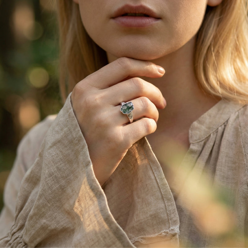 Woman wearing the sterling silver moss agate leaf ring on her finger in a natural outdoor setting.