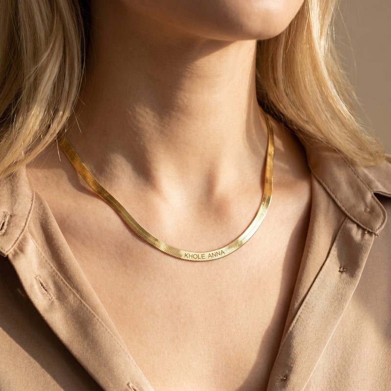 Model wearing the 18K gold finish custom name herringbone necklace with a tan shirt.