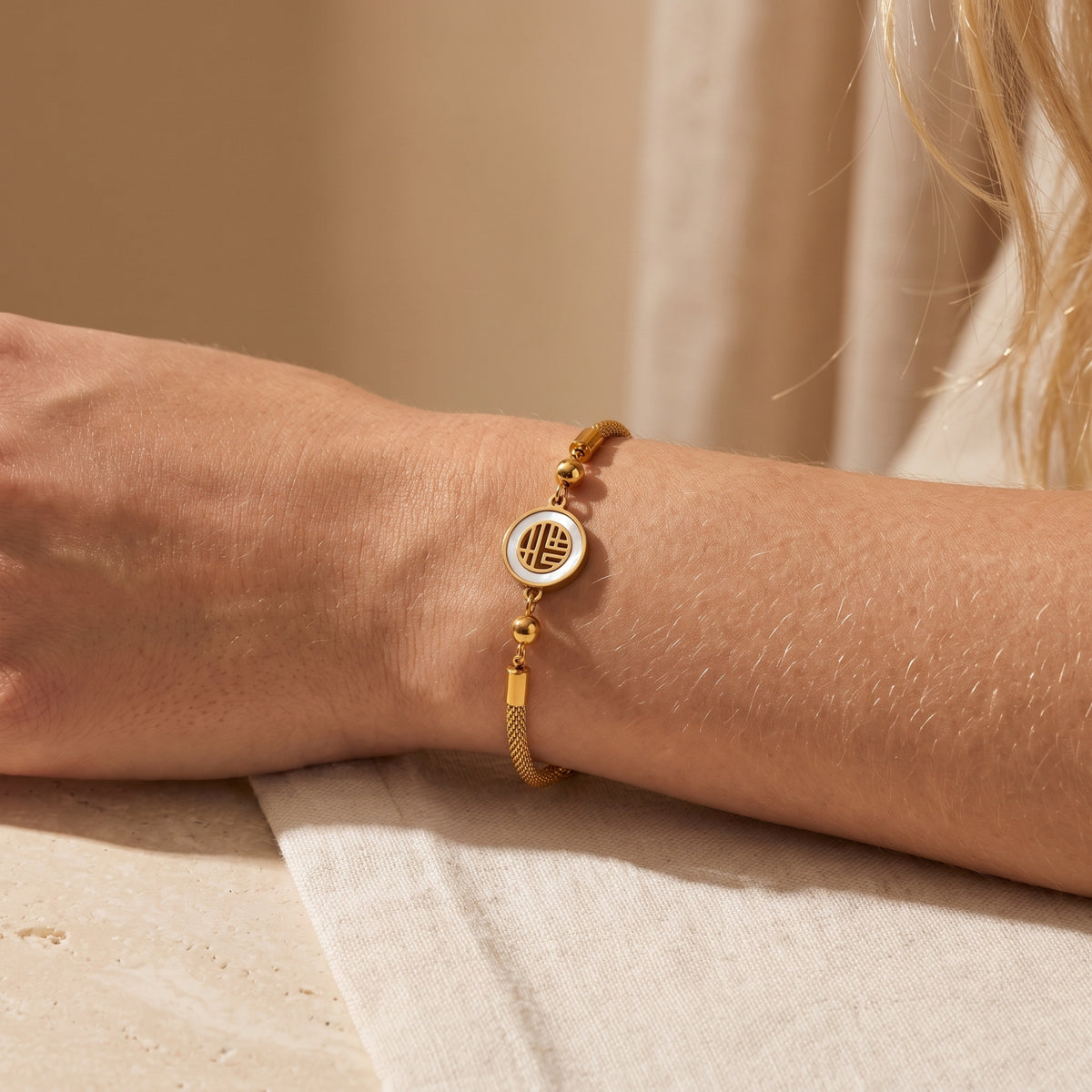Model wearing the gold-tone mesh bracelet with a round white inlay medallion on her wrist.