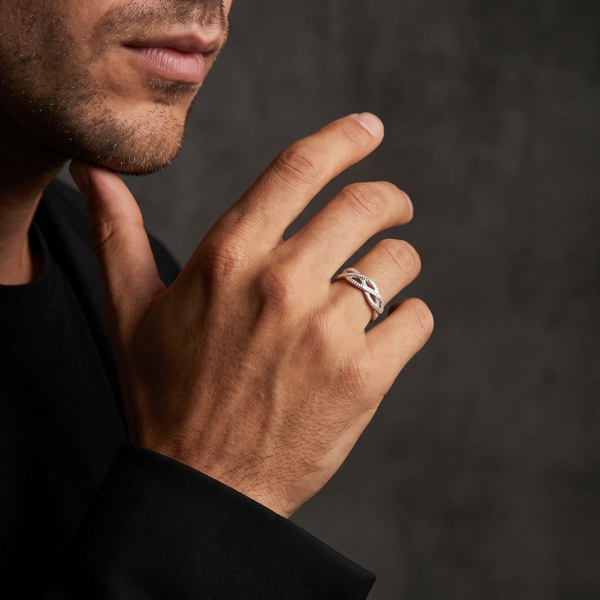 Model wearing the textured silver interlocking ring on the ring finger with a hand raised near the chin.