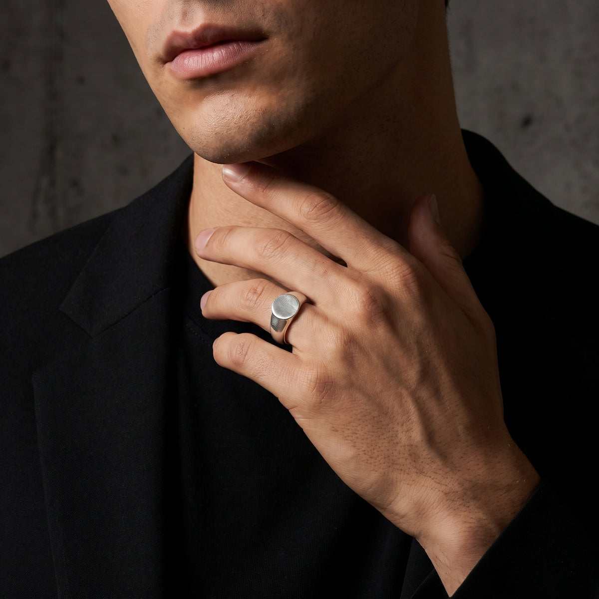 Model wearing the silver ring on a ring finger, with a hand raised near the neck against a dark backdrop.