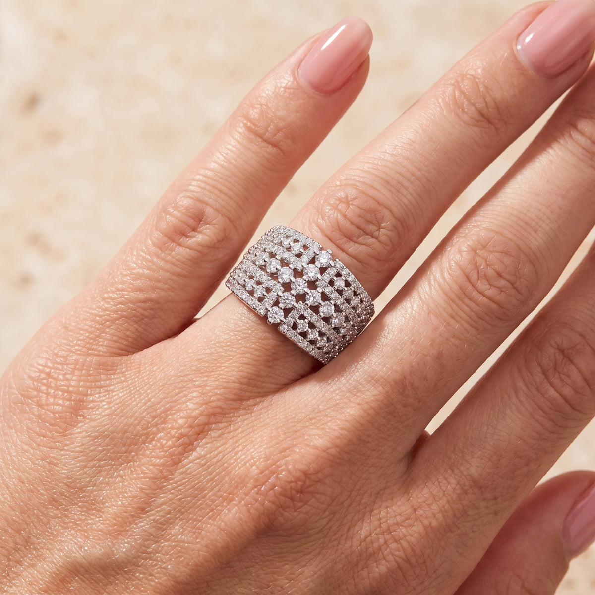 Wide silver lattice ring with round clear stones, shown worn on a finger in close-up.