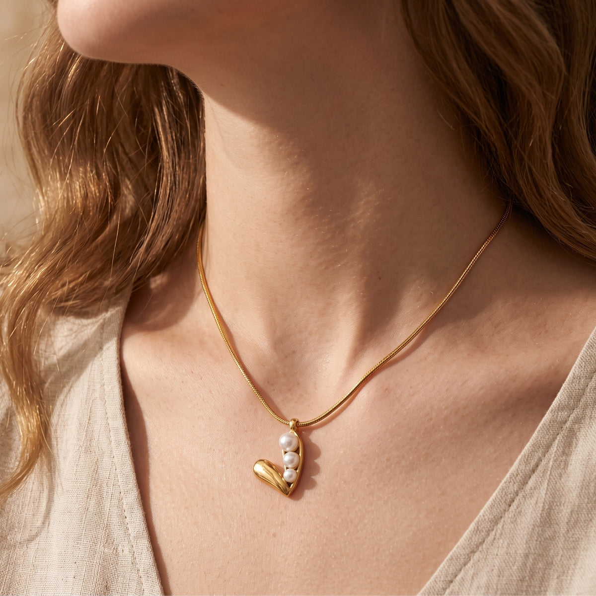 Side view of a model wearing the gold-tone snake-chain necklace with its three-pearl pod pendant.
