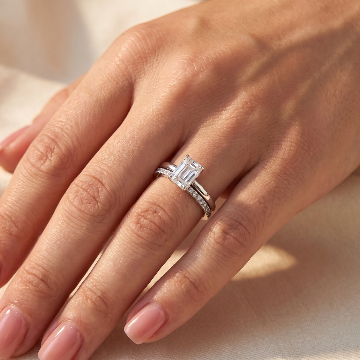 Close-up of a hand wearing the silver emerald-cut ring stacked with a clear pavé accent band.