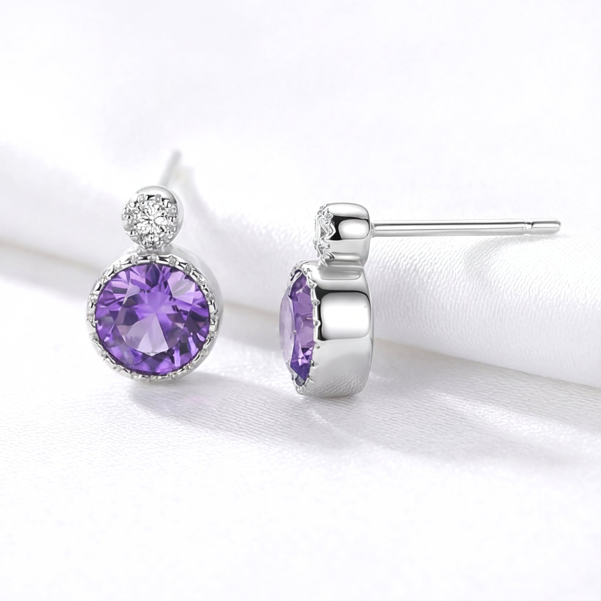 Front and side profile of round simulated amethyst stud earrings in S925 sterling silver on white fabric.