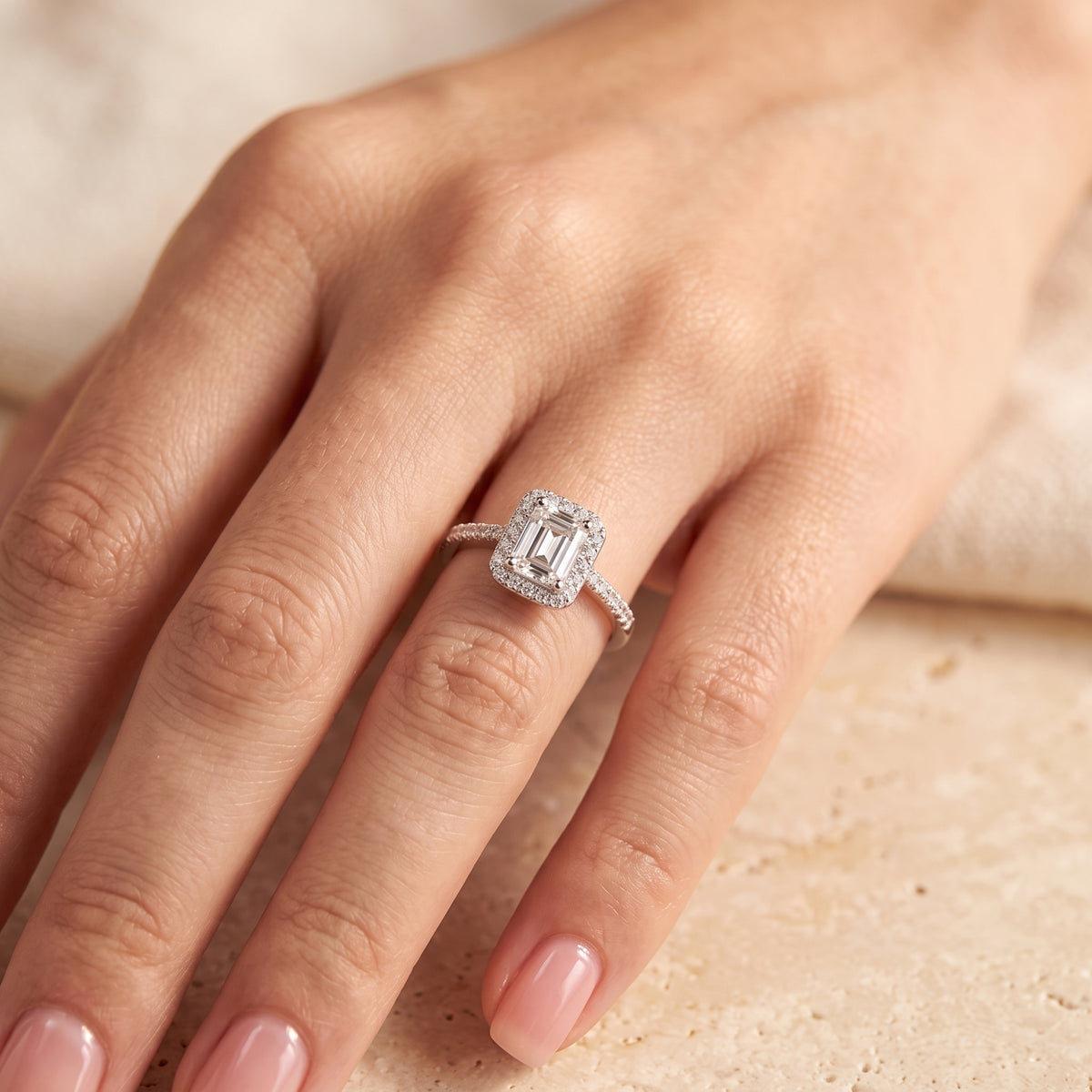 Top-down view of an emerald-cut halo ring with a pavé band worn on a hand.